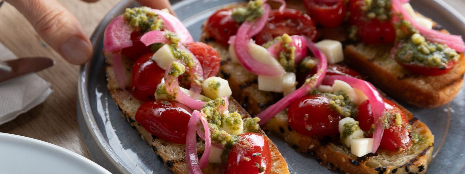 Vegetarian Menu Napier: Cherry Tomato Bruschetta - Fresh mozzarella with pickled onion, and basil pesto, on crisp bread.