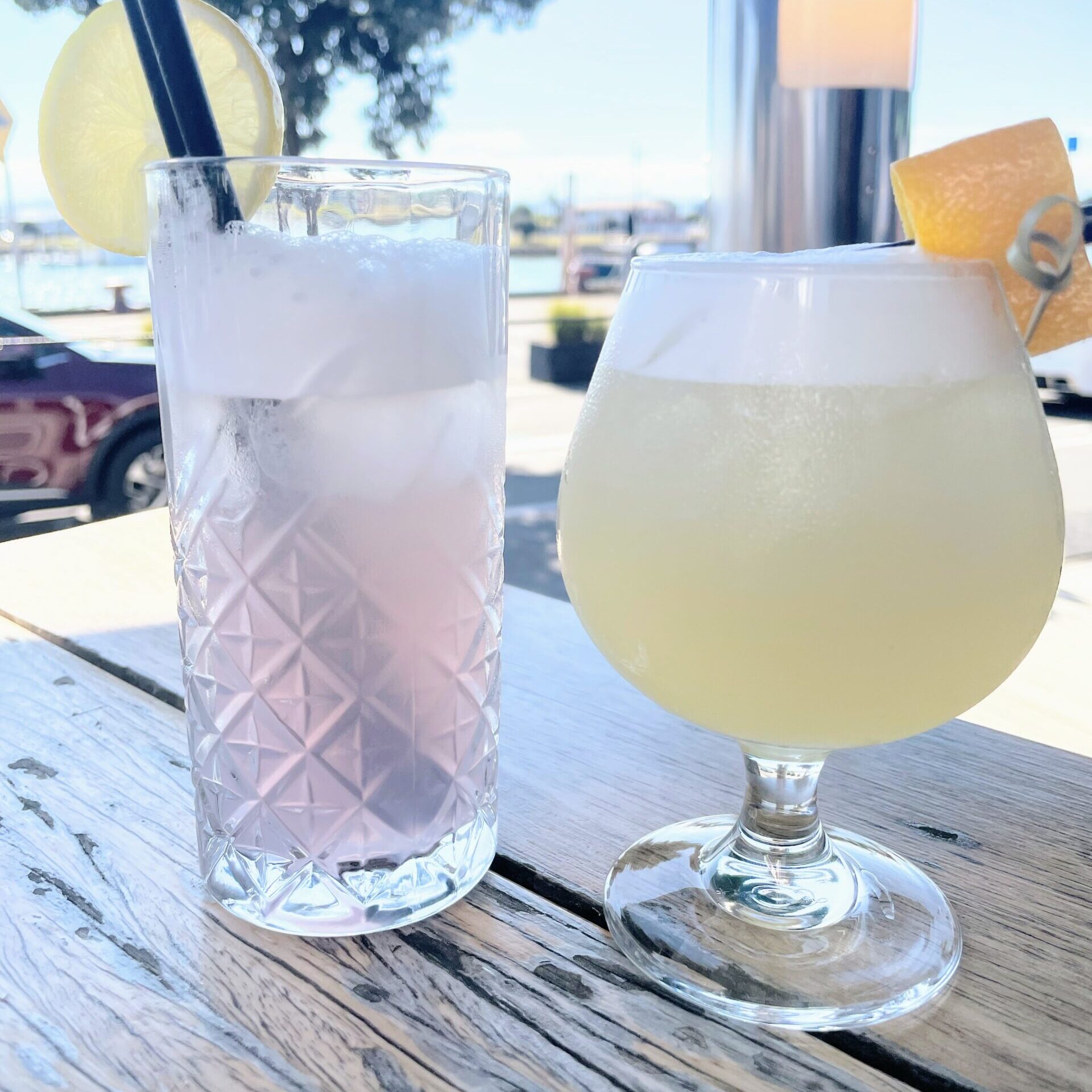 On the left in a Collins glass is a light pink Empress Fizz, on the right in a brandy balloon a light yellow gincello cocktail outside at Napier cocktail bar, The Gintrap.